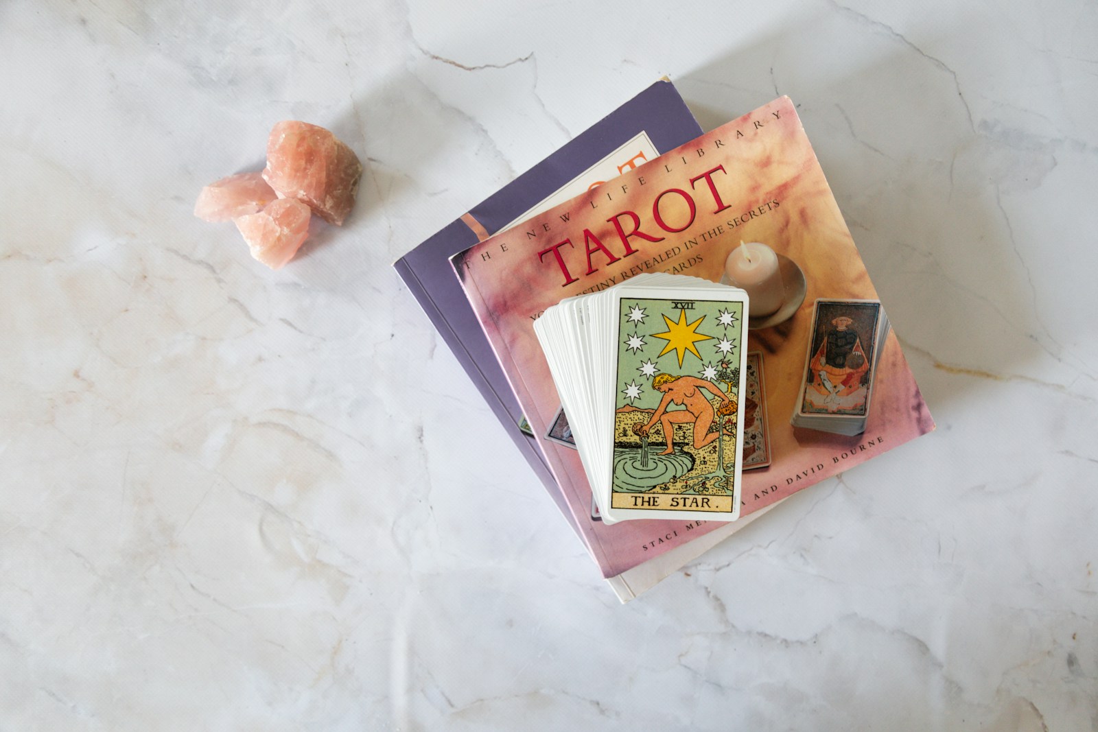 The Star tarot card rests atop tarot books and pink crystal pieces, symbolizing guidance and introspection in spiritual practices.