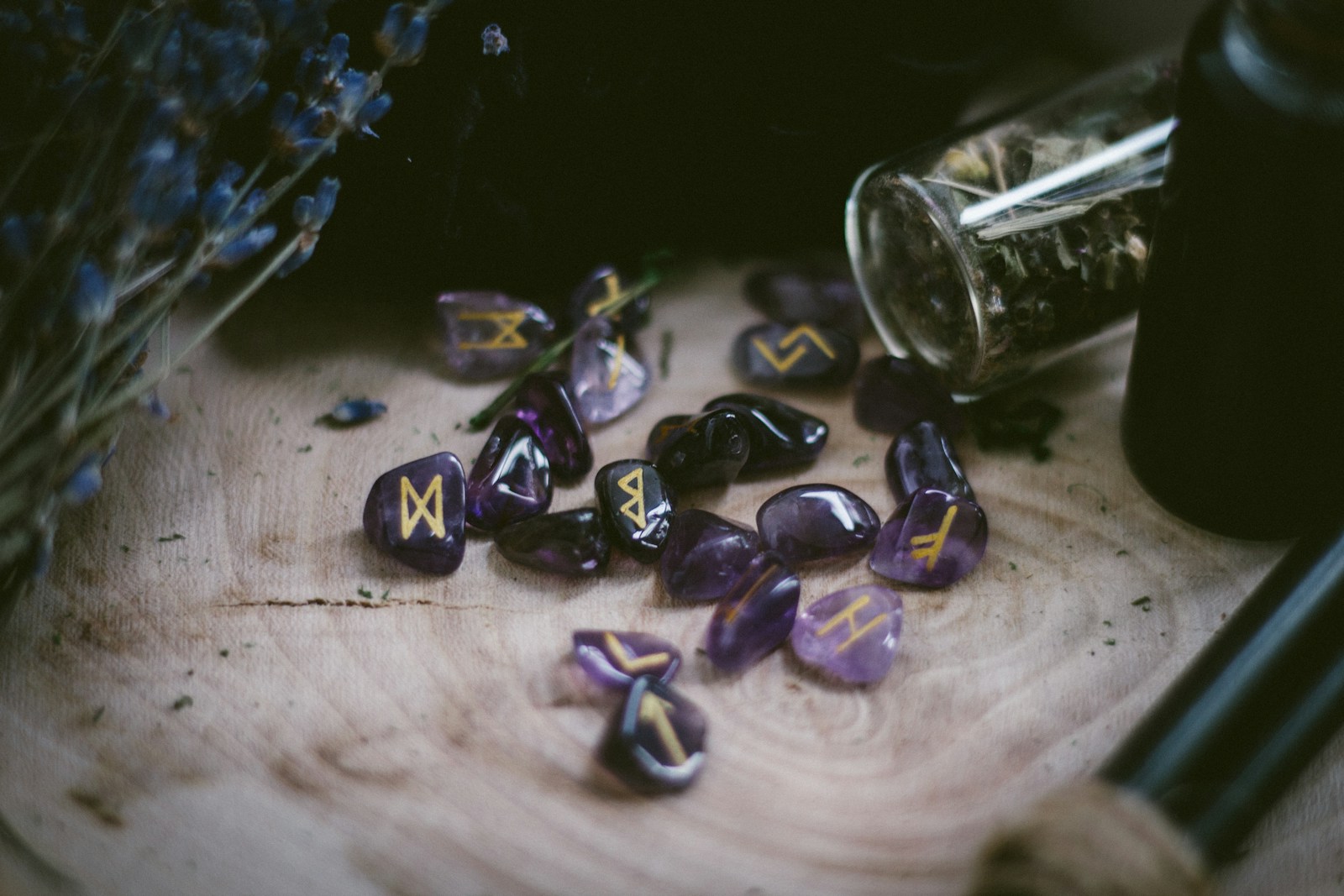 Purple crystal runes with golden markings scattered on a wooden surface, surrounded by dried lavender and herbal jars, evoking a mystical atmosphere.