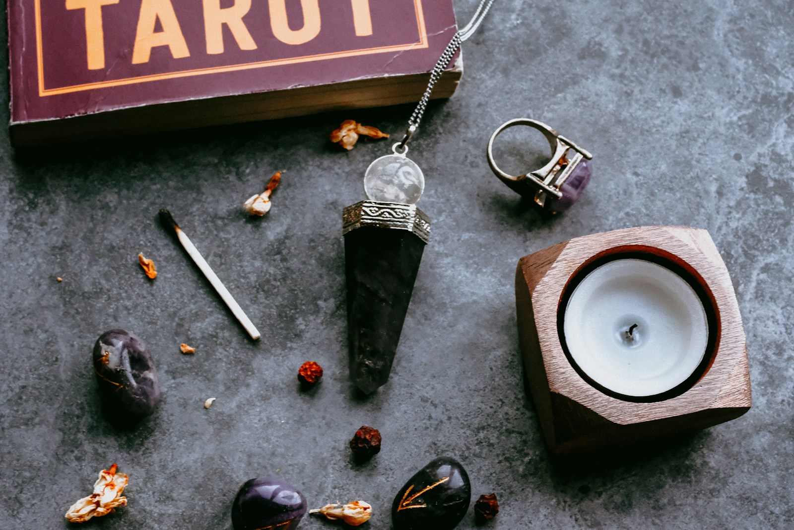 Tarot book, crystals, a pendulum, and a candle arranged on a textured surface, creating a mystical ambiance for divination practices.