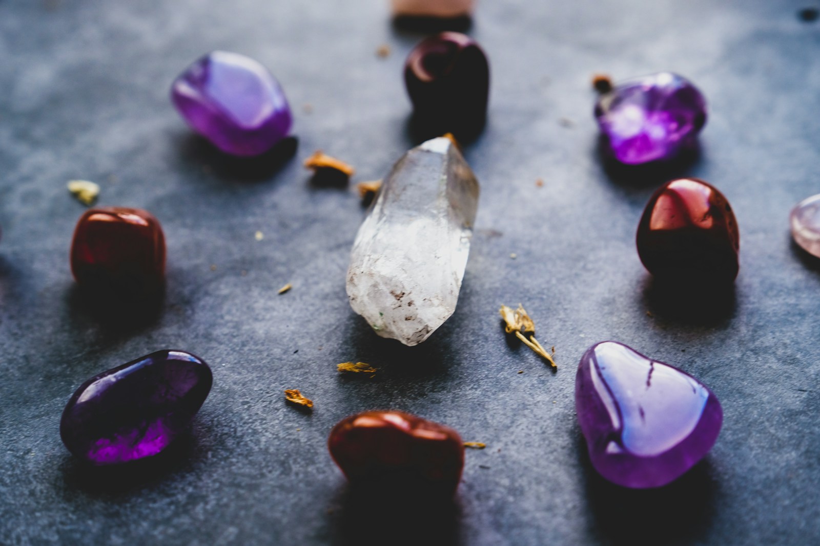 Collection of colorful gemstones, including amethyst and a clear quartz crystal, arranged artistically on a textured surface.